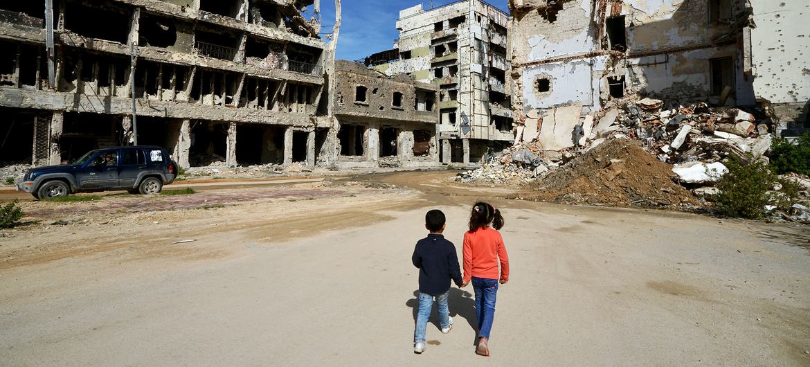 کودکان از کنار ساختمان های آسیب دیده در بنغازی در لیبی عبور می کنند.
