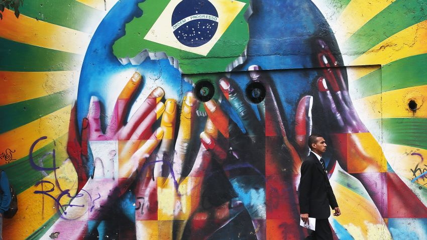 سائو پائولو، برزیل - 10 ژوئن: مردی در 10 ژوئن 2014 در سائوپائولو، برزیل، گرافیتی از دست های چند رنگی را که از سیاره علامت گذاری شده با پرچم برزیل حمایت می کند، عبور می دهد.  بازی افتتاحیه جام جهانی فوتبال 2014 در 12 ژوئن در سائوپائولو برگزار می شود که برزیل به مصاف کرواسی می رود.  (عکس از ماریو تاما/گتی ایماژ)